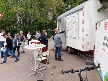 Mehrere Personen unterhalten sich rund um Stehtische und Pläne am Infowagen